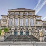 Großartiges historisches Gebäude mit Steinstufen, verzierten Säulen und Statuen. Blauer Himmel im Hintergrund.