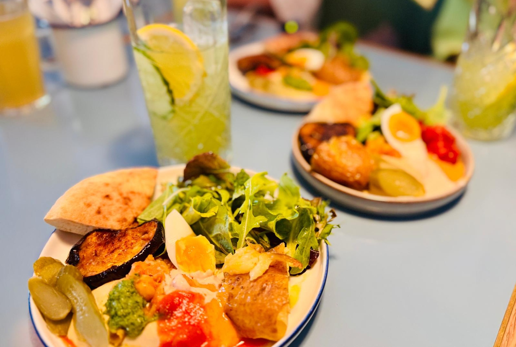 Platten mit Salat, Fladenbrot, gegrilltem Gemüse, Essiggurken und mit Zitrone und Minze garnierten Getränken - die perfekten Aromen für eine kulinarische Stadtführung durch Neukölln in Berlin.