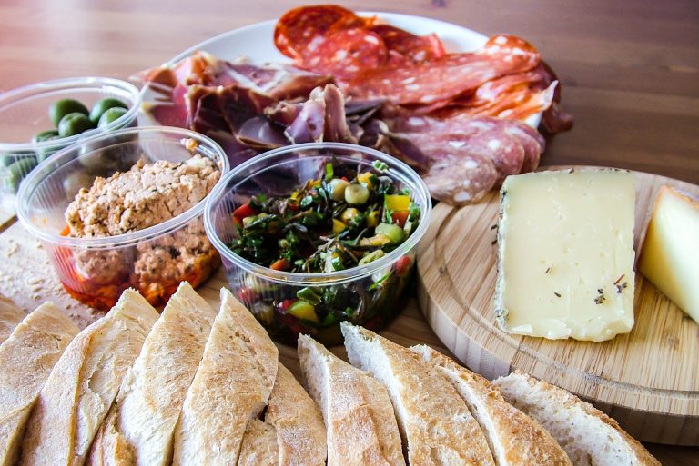 Aufgeschnittenes Brot, Käse, Wurstwaren, Oliven und Aufstriche auf einem Holztisch zu einer Wursttafel arrangiert - perfekt zum Genießen bei einer kulinarischen Stadtführung durch den Prenzlauer Berg.