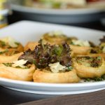 Ein köstlicher Teller mit herzhaftem Gebäck, belegt mit Kräutern und Käse, perfekt für jede Weihnachtsfeier, wird mit frischem Grün garniert auf einem rustikalen Holztisch serviert.