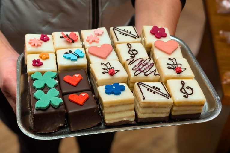 Ein Tablett mit dekorierten Petit Fours mit Blumen, Herzen, Schmetterlingen, Noten und Kleeblättern obenauf - perfekt für eine kulinarische Stadtführung in Bremen oder einen Spaziergang durch die charmante Bremer Altstadt.