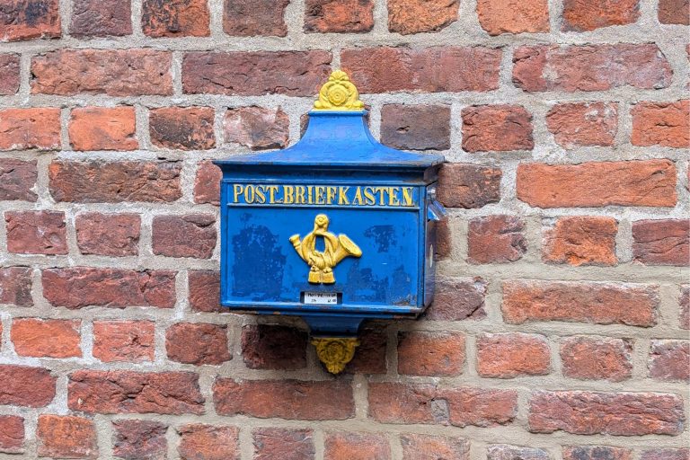 Ein blau-goldener Vintage-Briefkasten mit der Aufschrift "POSTBRIEFKASTEN" an einer roten Backsteinmauer, ein reizvoller Anblick, den man oft bei einer Stadtführung durch die malerische Bremer Altstadt entdeckt.