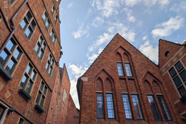 Backsteingotische Gebäude mit Spitzbögen und vielen Fenstern zieren die Bremer Altstadt vor einem blauen, wolkenverhangenen Himmel. Perfekt für eine Erkundungstour oder eine kulinarische Stadtführung durch dieses historische Viertel.