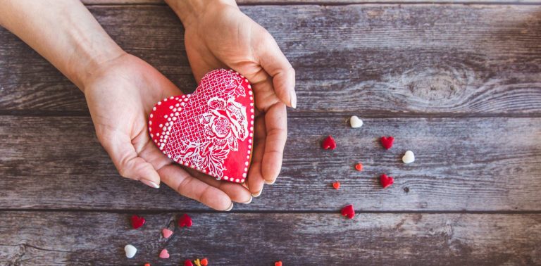 Valentine day gingerbread cookies heart in wooman hands with sprinkles on wooden background