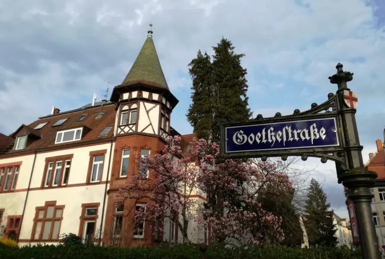 Im malerischen Freiburger Stadtteil Wiehre steht ein historisches Gebäude mit einem Turm neben einem blühenden Baum und einem Straßenschild mit der Aufschrift „Goethestraße“ – ein perfekter Ausgangspunkt für eine kulinarische Stadtführung.