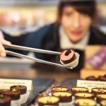 Eine Frau nimmt während einer kulinarischen Stadtführung in der Mannheimer Neckarstadt mit einer Zange ein Schokoladendessert aus einer Auslage mit verschiedenen Pralinen auf.