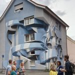 Eine Gruppe von Menschen steht vor einem Gebäude in der Mannheimer Neckarstadt, dessen Fassade mit großer, blauer, abstrakter 3D-Straßenkunst verziert ist.
