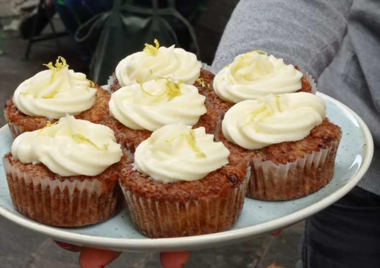 Ein Teller mit sechs Cupcakes mit weißem Zuckerguss und Zitronenschale, gehalten von einer Person, perfekt für eine kulinarische Stadtführung Mannheims durch die lebendigen Straßen des Mannheimer Jungbusch.