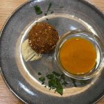 Ein Falafelbällchen mit Soße, Dip und gehackten Kräutern auf einem grauen Teller auf einem Holztisch - perfekt zum Probieren bei einer Kulinarischen Stadtführung Mannheim durch den lebendigen Jungbusch oder das historische Quadrate.