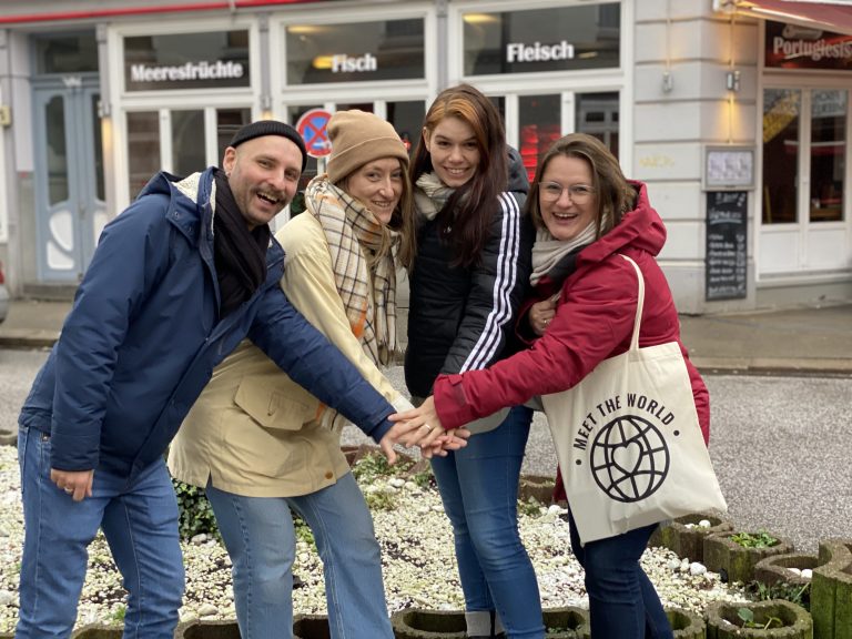 Vier Personen lächeln und legen ihre Hände ineinander während einer Stadterkundung in München.