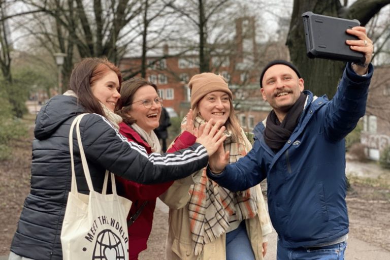 Vier Menschen, die lächeln und im Historischen Zentrum von Hamburg während eines Outdoor-Escape-Games an einem bewölkten Tag im Park ein Gruppen-Selfie machen.