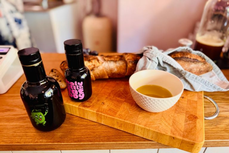 Zwei Flaschen, eine Schale mit Öl und ein Baguette auf einem hölzernen Schneidebrett erinnern an das kulinarische Flair von Berlin-Neukölln in einer gemütlichen Küchenumgebung.