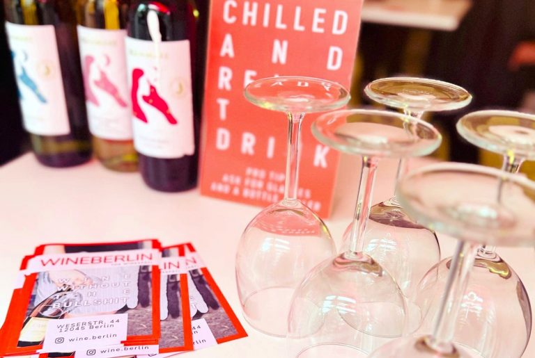 Weinflaschen, umgedrehte Weingläser und Flyer auf einem Tisch mit einem "Chilled and Ready to Drink"-Schild - perfekt für eine kulinarisch vegane Stadtführung in Berlin Neukölln.
