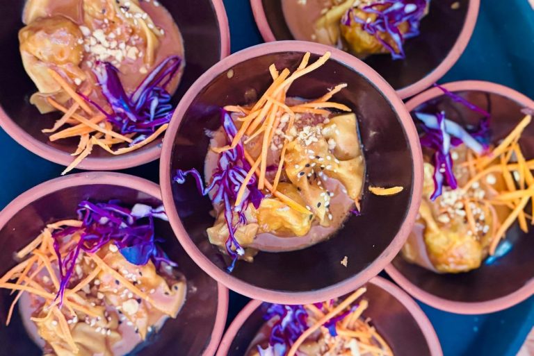 Kleine Schalen mit Knödeln, die mit Erdnusssauce, geraspelten Karotten, lila Kohl und Sesam belegt sind - perfekt für eine vegane Stadtführung durch den lebendigen Prenzlauer Berg.