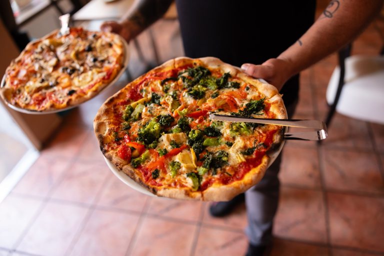 Eine Person mit zwei Pizzatellern, einer mit Gemüse und einer mit Pilzen belegt, in einem gemütlichen Restaurant im Kölner Agnesviertel - perfekt für eine kulinarische Stadtführung durch die Stadt.