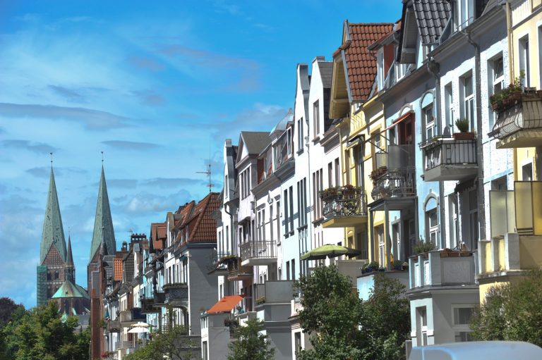 Bunte europäische Stadthäuser mit Balkonen säumen eine Straße in Lübeck St. Jürgen, im Hintergrund erheben sich Kirchtürme unter blauem Himmel - wie geschaffen für eine kulinarische Stadtführung Lübeck oder Stadtführung St. Jürgen.