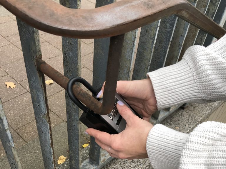 Hände versuchen eifrig, ein Schließfach zu öffnen, das an einem rostigen Geländer im Freien befestigt ist, und legen die darin verborgenen Frühlingshighlights frei.