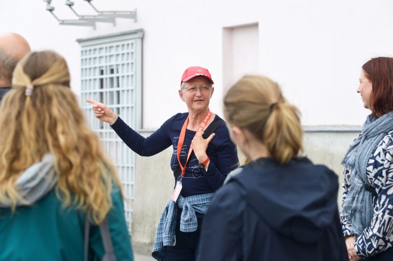 Der Reiseleiter mit der roten Mütze gibt der kleinen Gruppe, die sich draußen um ihn versammelt hat, begeistert Einblicke und weist auf Frühlingshighlights hin.