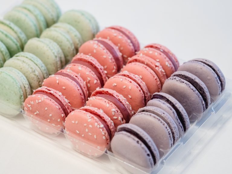 Pastellgrüne, rosafarbene und violette Macarons von Oostal reihen sich in einer durchsichtigen Plastikschale auf einer weißen Fläche aneinander - der perfekte Genuss nach einer Baden-Baden Kulinarische Aktiv-Tour.