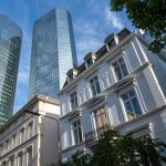 Unter blauem Himmel erheben sich im Frankfurter Westend moderne gläserne Wolkenkratzer hinter historischen weißen Gebäuden, mit etwas Grün im Vordergrund - eine ideale Kulisse für eine kulinarische Stadtführung durch dieses lebendige Viertel.
