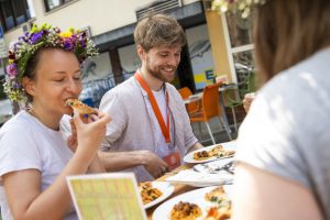 Drei Personen genießen Pizza unter freiem Himmel in Hamburg; eine Frau trägt eine Blumenkrone, was dieses Essen zu einem der charmanten romantischen Dates oder perfekten Date-Ideen macht, die Hamburg bietet.