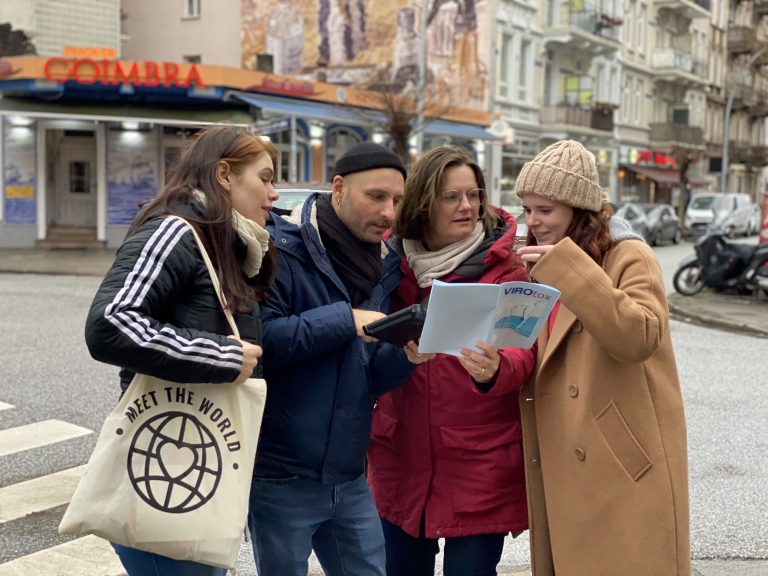 Vier Menschen stehen auf einer Straße in der Stadt, schauen auf einen Stadtplan und ein Tablet und scheinen gemeinsam zu navigieren, während sie spannende aktivitäten münchen planen.