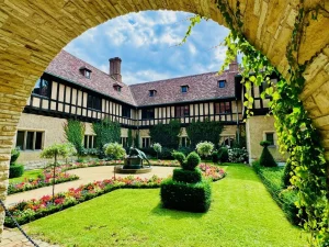 Ein üppiger Gartenhof mit gepflegten Hecken und Blumen, umrahmt von einem steinernen Torbogen und einem historischen Gebäude, erinnert an die Eleganz der Schlösser Potsdam und an den Charme der berühmten Parks Potsdam.