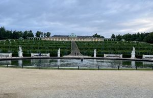 Barockes Schloss mit terrassenförmig angelegten Gärten, Statuen und einem kreisrunden Teich unter wolkenverhangenem Himmel - eines der Top-Schlösser Potsdams und ein Muss für die Sehenswürdigkeiten Potsdams.