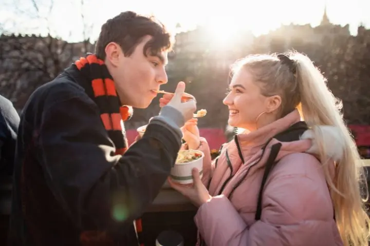 Zwei Menschen, die sich im Freien aufhalten, Essen teilen und sich im Sonnenlicht anlächeln - die perfekte Inspiration für date ideen Hamburg.