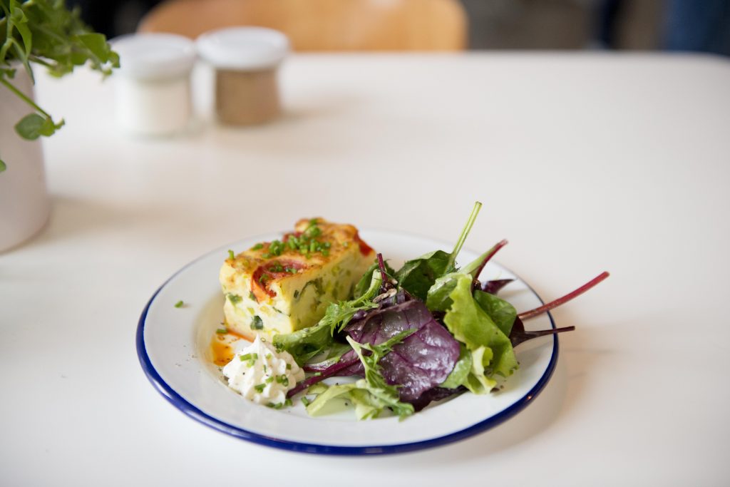 Ein Teller mit Quiche, gemischtem Grünzeug und einem Klecks cremigem Salat auf einem weißen Tisch - perfekt für Ihr nächstes Date.