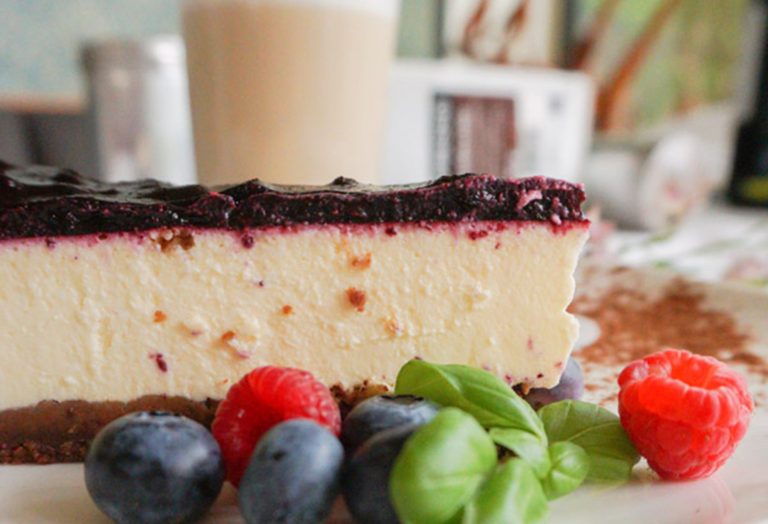 Scheibe Käsekuchen mit Beeren-Topping, Heidelbeeren, Himbeeren und Basilikumblättern an der Seite - perfekt für einen süßen Zwischenstopp bei einer kulinarischen Stadtführung in Köln oder Mülheim.
