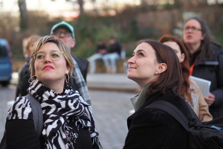 Zwei Frauen lächeln und schauen nach oben, während sie einen echten Entdecker-Genießer-Tag in Potsdam genießen, mit einer Gruppe von Menschen im Hintergrund.