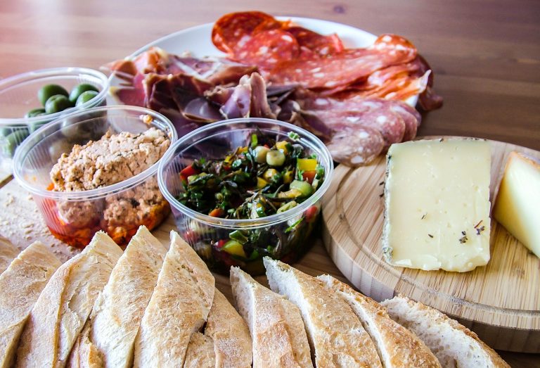 Aufgeschnittenes Brot, Käse, Wurst, Oliven und Dips, angerichtet auf einem Holzbrett und einem Teller - perfekt für einen Entdecker-Genießer-Tag in Potsdam.