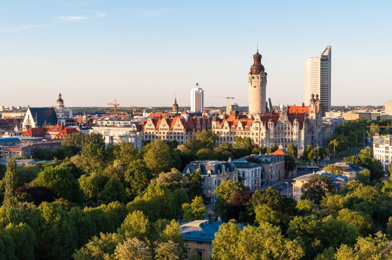 Ein Stadtbild von Leipzig, Deutschland, mit historischen Gebäuden, modernen Wolkenkratzern und grünen Bäumen bei Sonnenuntergang - perfekt für Entdecker und Genießer nach einem Tag in der Nähe von Potsdam.