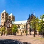 Der historische Münsterdom mit seinen Zwillingstürmen und seiner gotischen Architektur steht stolz in der Altstadt, umgeben von Bäumen und einem großen Platz.