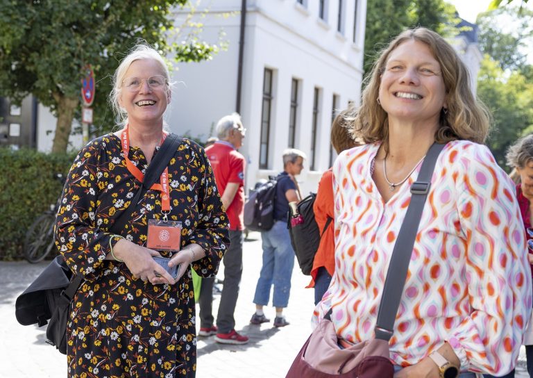 Zwei lächelnde Frauen stehen an einem sonnigen Tag im Freien während einer kulinarischen Stadtführung in der Nürnberger Altstadt, mit einer Gruppe von Menschen im Hintergrund.