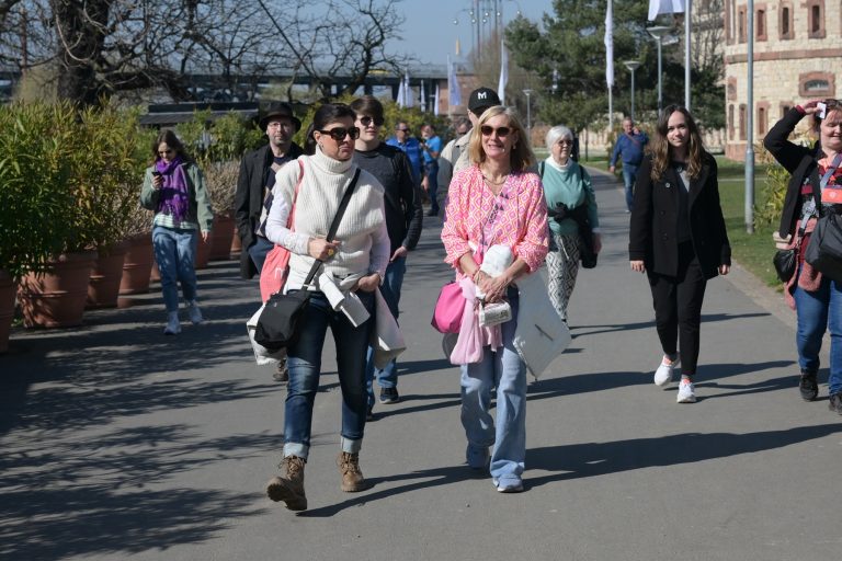 Eine Gruppe von Menschen geht an einem sonnigen Tag in der Südlichen Altstadt von Mainz im Freien spazieren, einige tragen Taschen und Sonnenbrillen und genießen eine kulinarische Stadtführung.