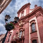 Barocke Kirchenfassade mit Statuen und Straßenlaternen unter einem dramatischen, wolkenverhangenen Himmel in der Südlichen Altstadt von Mainz, perfekt zu bewundern während einer Kulinarischen Stadtführung.