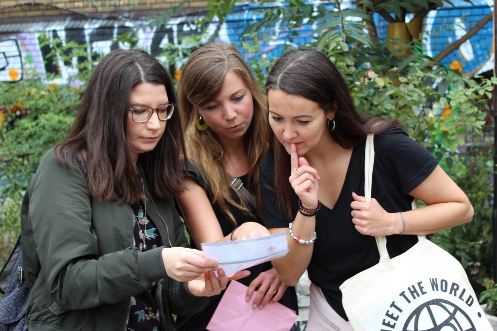 Beim Mikroabenteuer erkunden drei Frauen die Stadt auf spielerische Weise, analysieren Hinweise und erleben gemeinsam spannende Entdeckungen in kreativer urbaner Umgebung.