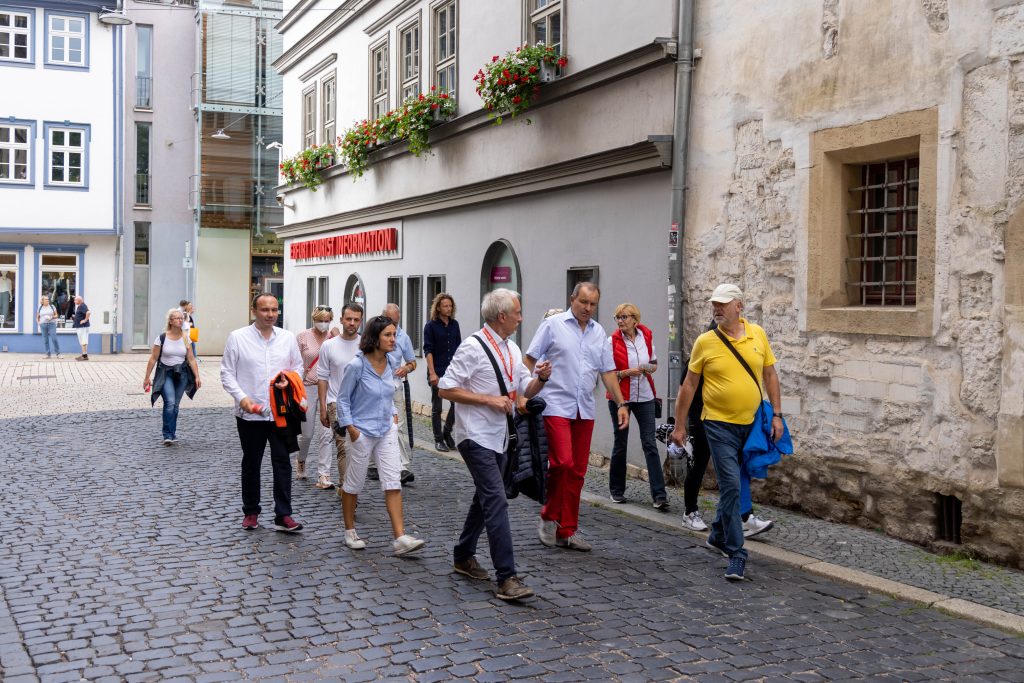 Eine Gruppe von Menschen genießt ihren Urlaub zu Hause, während sie gemeinsam durch die Kopfsteinpflasterstraßen einer charmanten europäischen Stadt schlendern.