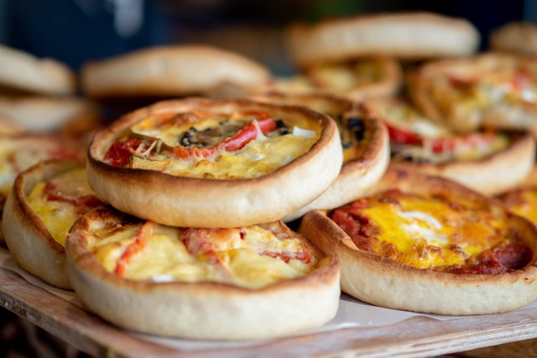 Ein Stapel kleiner, runder Pizzen mit verschiedenen Belägen auf einer hölzernen Unterlage - perfekt zum Teilen während einer kulinarischen Stadtführung in Hoheluft, Hamburg.