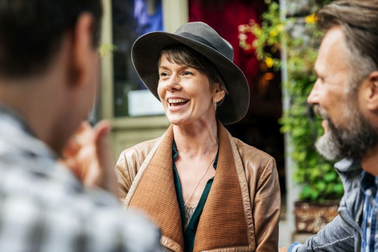 Eine Frau mit Hut lächelt, während sie sich während einer kulinarischen Stadtführung im pulsierenden Hamburger Stadtteil Hoheluft mit zwei Personen unterhält.