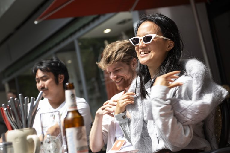 Drei Personen sitzen an einem sonnigen Tag beim Tagesausflug Münster draußen an einem Tisch, lachen und genießen Getränke.