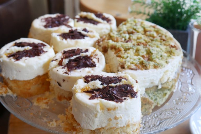 Mini-Kuchen mit Schlagsahne und Schokoladenraspeln auf einem Glasteller, im Hintergrund ein Streuselkuchen – perfekte Köstlichkeiten, die man bei einer kulinarischen Stadtführung durch Dortmunds charmantes Kreuzviertel entdecken kann.