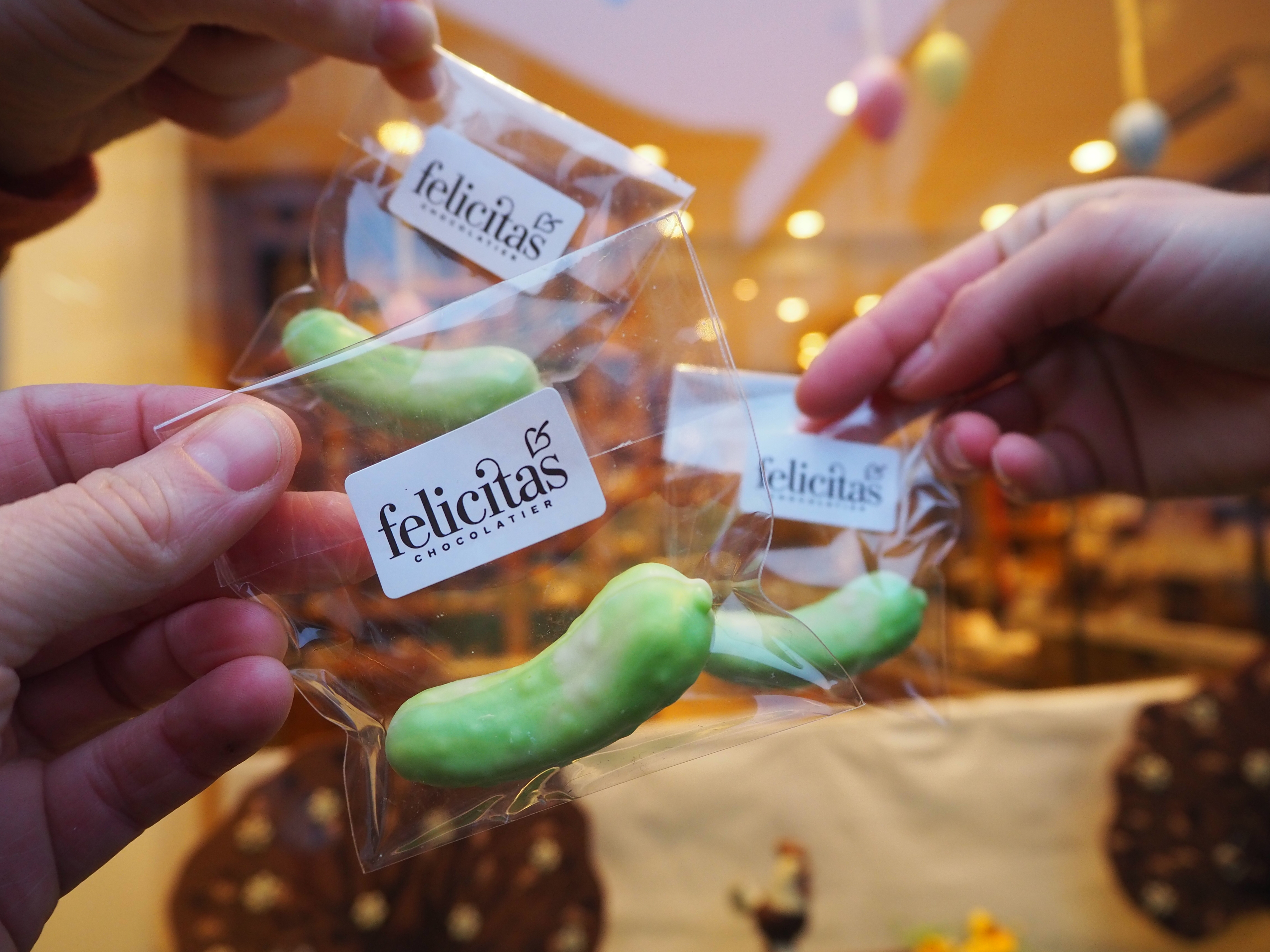 Drei Hände halten durchsichtige Tüten mit grünen Schokoladenleckereien und Etiketten mit der Aufschrift „felicitas chocolatería“ – perfekte süße Mitbringsel von einem Tagesausflug nach Potsdam.