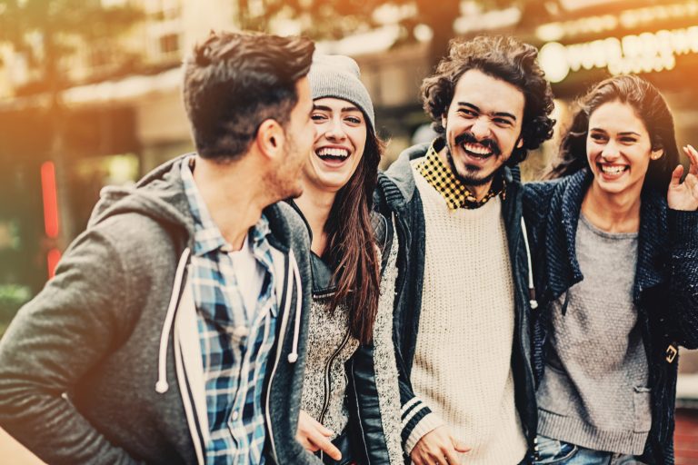 Vier Freunde in Freizeitkleidung lachen an einem sonnigen Tag gemeinsam im Freien, die Arme um die Schultern des anderen gelegt, und genießen die lebhafte Atmosphäre des Michaelisviertels während einer kulinarischen Stadtführung.