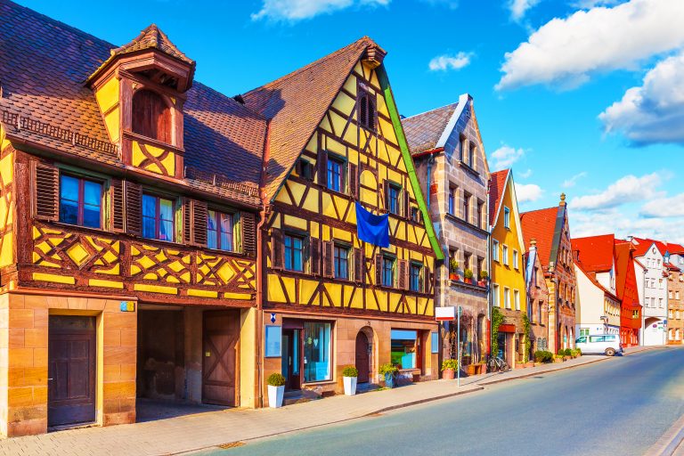 Im charmanten Michaelisviertel säumen bunte Fachwerkhäuser eine ruhige Straße unter blauem Himmel mit vereinzelten Wolken und laden Besucher dazu ein, das einzigartige Flair des Viertels zu entdecken – vielleicht im Rahmen einer kulinarisch-veganen Stadtführung durch Fürth.