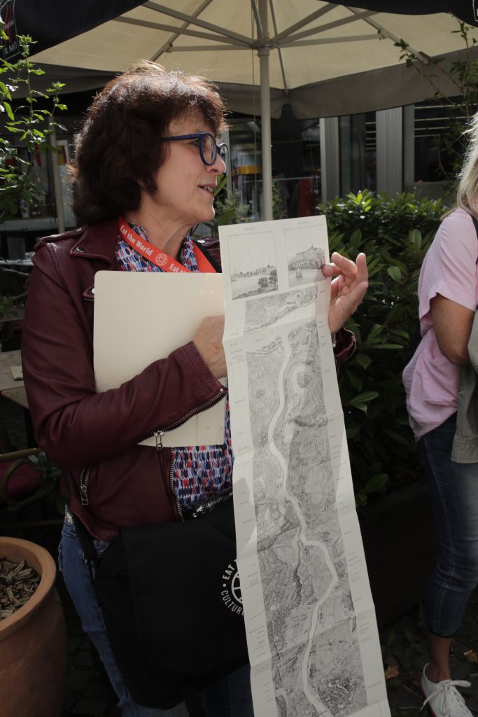 Eine Frau hält eine lange, schwarz-weiß illustrierte Karte von Frankfurt in der Hand und bespricht sie im Freien unter einem Regenschirm.
